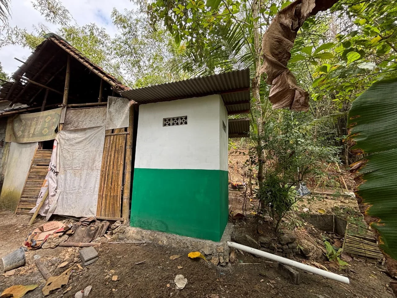 Bangunan jamban sehat di lingkungan rumah warga dengan latar pepohonan dan permukiman sekitar