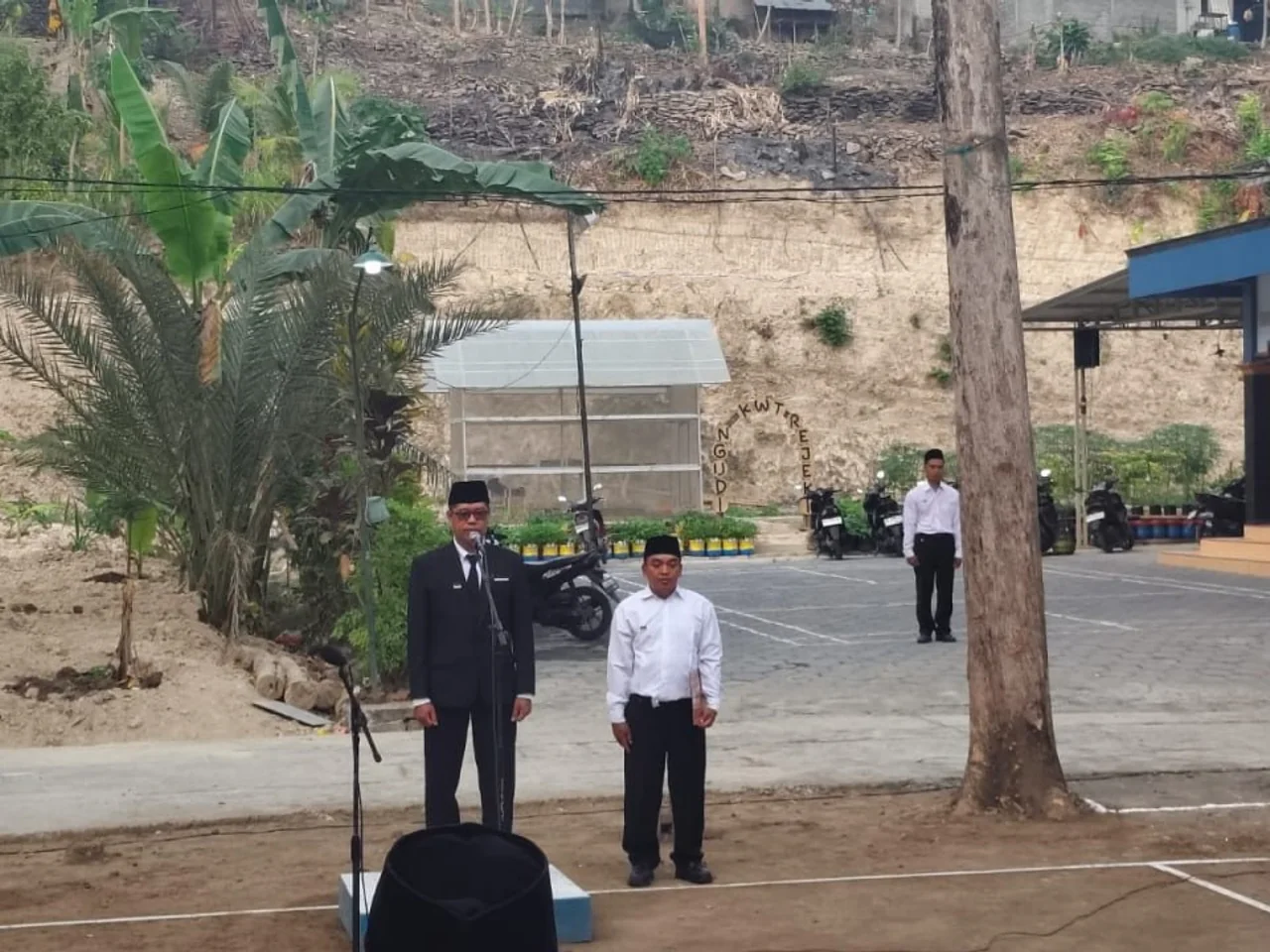 Inspektur upacara berdiri di depan mikrofon bersama petugas upacara di Lapangan Voli RT 01 Banyu Temumpang